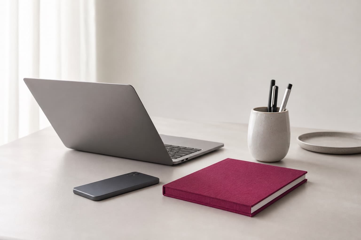 Stillleben: Laptop, Smartphone und Stifte mit beerenrotem Notizbuch